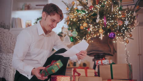 Glücklicher-Mann-Hält-Ein-Weihnachtsgeschenk-In-Der-Hand,-Während-Er-Zu-Hause-Einen-Brief-Liest