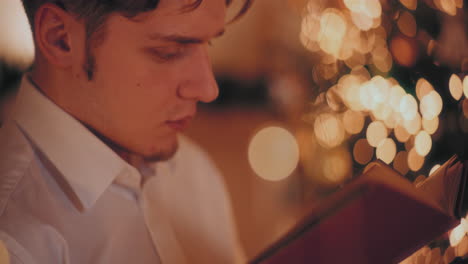 Hombre-Leyendo-Un-Libro-En-Casa-Iluminada-Durante-La-Navidad