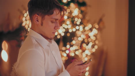 Mann-Benutzt-Smartphone-Zu-Weihnachten-Im-Beleuchteten-Haus