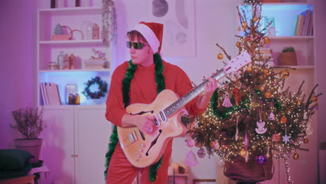 Man-playing-guitar-by-decorated-Christmas-tree-at-home