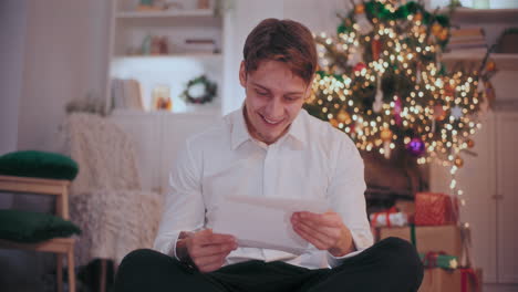 Hombre-Feliz-Leyendo-Una-Carta-Mientras-Está-Sentado-En-Casa-Durante-La-Navidad
