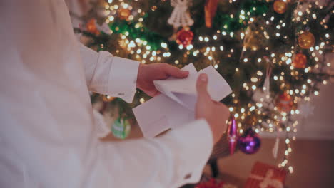Man-opening-letter-with-decorated-Christmas-tree-in-background