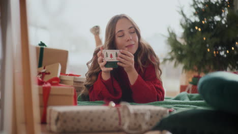 Entspannte-Frau-Hält-Während-Weihnachten-Eine-Kaffeetasse-In-Der-Hand,-Während-Sie-Auf-Dem-Boden-Liegt