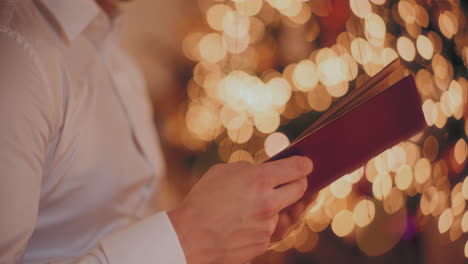 Man-holding-book-against-illuminated-Christmas-tree