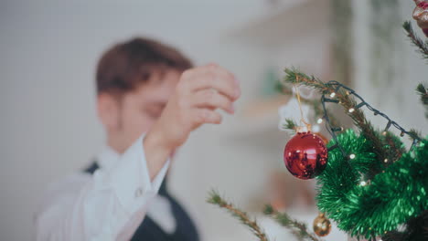 Schöner-Mann,-Der-Eine-Rote-Kugel-An-Den-Beleuchteten-Weihnachtsbaum-Hängt