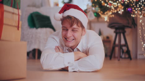 Amazed-man-in-Santa-hat-sliding-Christmas-gifts-while-lying-on-floor