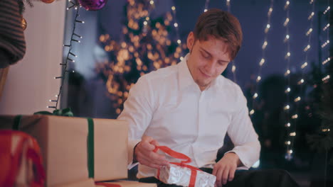Man-opening-Christmas-gift-after-reading-letter-at-illuminated-home