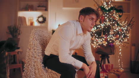 Deprimierter-Mann-Hält-Weihnachtsmütze-In-Der-Hand,-Während-Er-Während-Weihnachten-Auf-Einem-Stuhl-Sitzt