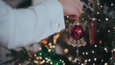 Hand-hanging-red-shiny-bauble-on-Christmas-tree-at-home