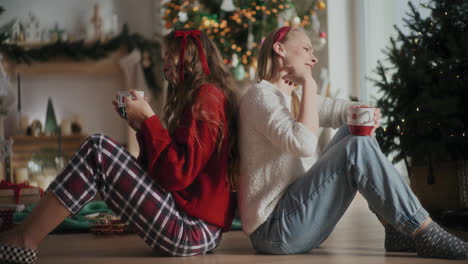 Fröhliche-Schwestern-Singen-Und-Genießen-Kaffee,-Während-Sie-Zu-Weihnachten-Auf-Dem-Boden-Sitzen