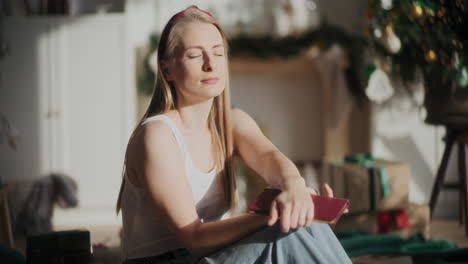 Woman-with-eyes-closed-holding-book-at-sun-lit-home-during-Christmas