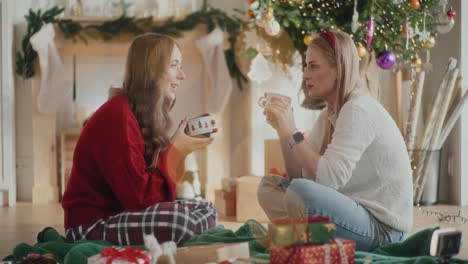 Hermosas-Hermanas-Hablando-Mientras-Sostienen-Tazas-De-Café-Durante-La-Navidad-En-Casa.