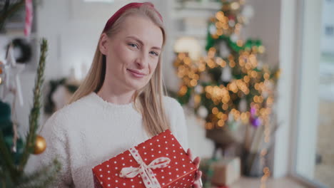 Cheerful-woman-holding-wrapped-Christmas-present-at-home