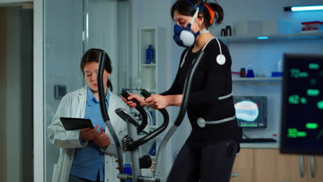 Woman-athlete-with-mask-running-on-cross-trainer-in-sports-science-lab