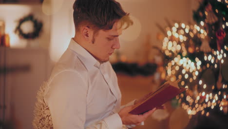 Hombre-Leyendo-Un-Libro-En-Casa-Iluminada-Durante-La-Navidad