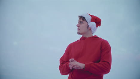 Thoughtful-man-in-red-hooded-jacket-and-Santa-hat-looking-away-against-sky