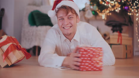 Happy-man-in-Santa-hat-sliding-Christmas-presents-while-lying-on-floor