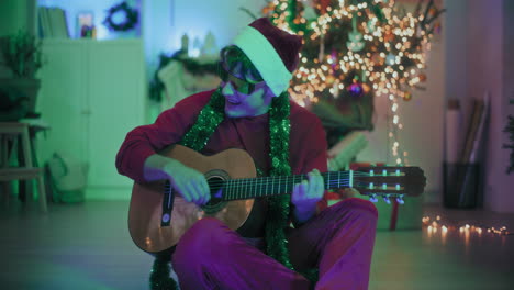 Mann-Spielt-Gitarre,-Während-Er-Zu-Weihnachten-Auf-Dem-Boden-Eines-Beleuchteten-Hauses-Sitzt