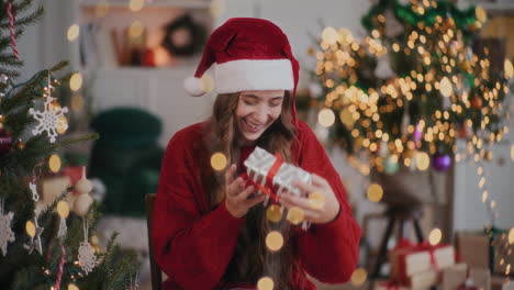 Aufgeregte-Frau-Mit-Weihnachtsmütze-Spielt-Mit-Geschenkbox-Im-Dekorierten-Zuhause