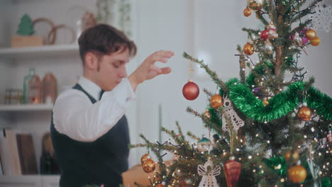 Un-Hombre-Guapo-Colgando-Adornos-Rojos-En-El-árbol-De-Navidad-En-Casa