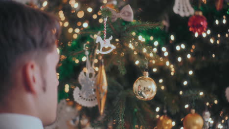 Man-hand-hanging-golden-shiny-bauble-on-illuminated-Christmas-tree