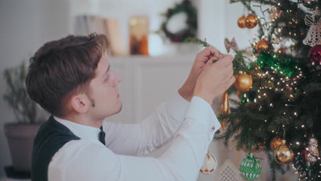 Well-dressed-man-hanging-bauble-on-Christmas-tree-at-home