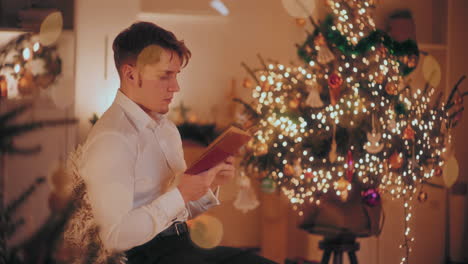 Un-Hombre-Guapo-Leyendo-Un-Libro-Mientras-Está-Sentado-En-Una-Silla-En-Casa-Durante-La-Navidad