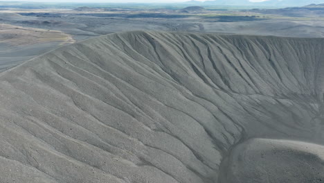 Volcano-crater-with-black-sand-and-scenic-landscape-in-the-background,-aerial