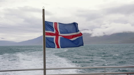 Island-Flagge-Auf-Einem-Fahrenden-Boot-Im-Meer,-Dem-Land-Aus-Feuer-Und-Eis,-Handheld