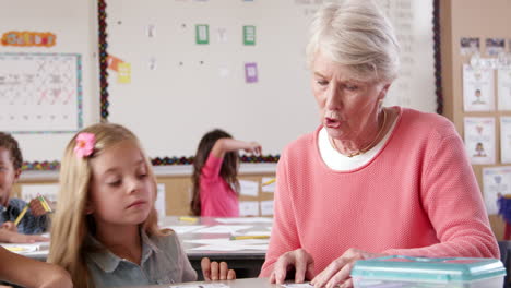 Senior-teacher-helping-young-schoolgirl-in-classroom