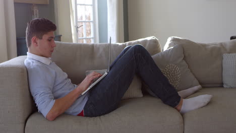 Teenage-Boy-Sitting-On-Sofa-Using-Laptop-At-Home-Shot-On-R3D