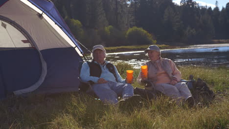 Senior-couple-sitting-outside-tent-near-lake,-closer-in-shot