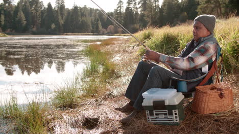 Senior-black-man-on-a-camping-trip-fishing-by-a-rural-lake