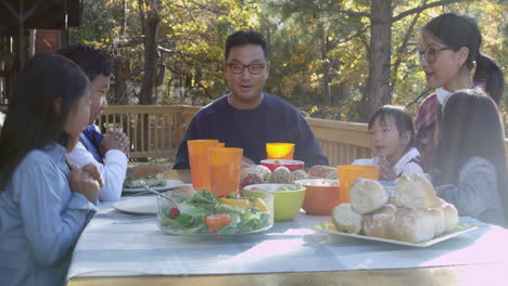 Asian-family-at-a-table-on-a-deck-say-a-prayer-before-eating,-shot-on-R3D
