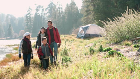 Parents-on-a-camping-trip-with-two-kids-walking-near-a-lake