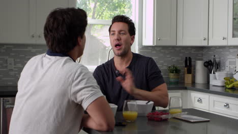 Male-gay-couple-talking-at-breakfast-in-their-kitchen,-shot-on-R3D