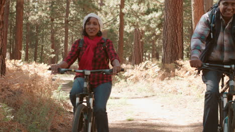 Senior-black-couple-cycle-past-camera-on-a-forest-trail