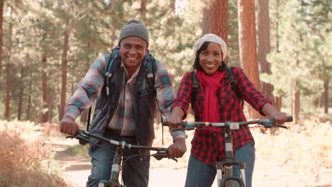 Senior-black-couple-sitting-on-bikes-in-a-forest,-close-up