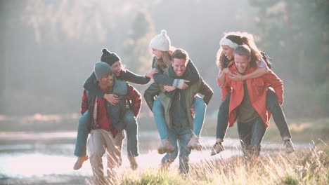 Six-friends-have-fun-piggybacking-in-the-countryside-by-lake