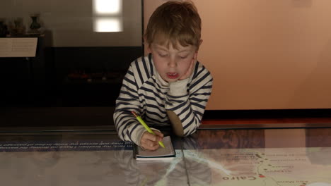 Boy-In-Museum-Studies-Map-And-Writes-In-Notebook-Shot-On-R3D