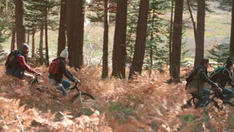 Friends-riding-bikes-in-forest,-side-view,-left-to-right-pan