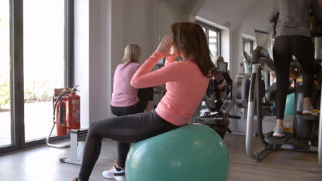 Woman-doing-crunches-on-a-fitness-ball-at-a-gym,-side-view