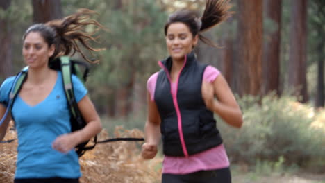 Two-young-women-running-in-a-forest,-close-up