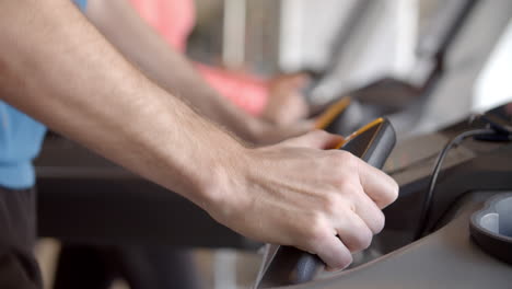 Man-pressing-buttons-on-a-running-machine-at-gym,-detail