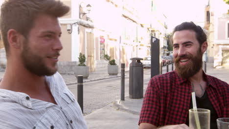 Two-male-friends-talking-at-a-table-outside-a-cafe,-Ibiza,-shot-on-R3D