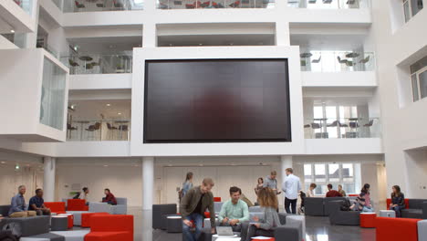Students-and-AV-screen-in-atrium-at-a-university,-tilt-shot