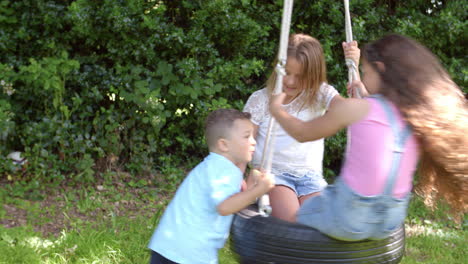 Group-Of-Children-Playing-On-Tire-Swing-In-Garden