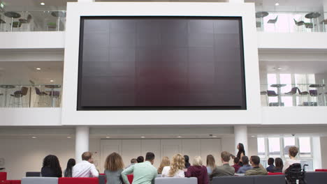 Students-at-a-lecture-watch-a-big-screen-in-a-university-atrium,-shot-on-R3D