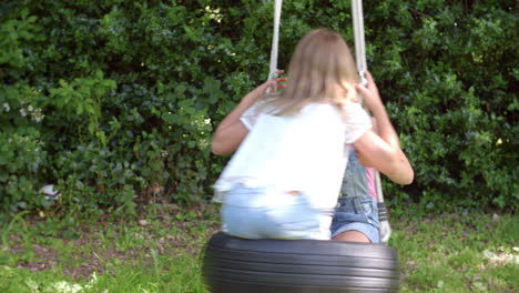 Two-Girls-Playing-On-Tire-Swing-In-Garden