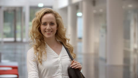 Blonde-female-university-student-walking-into-focus-in-lobby